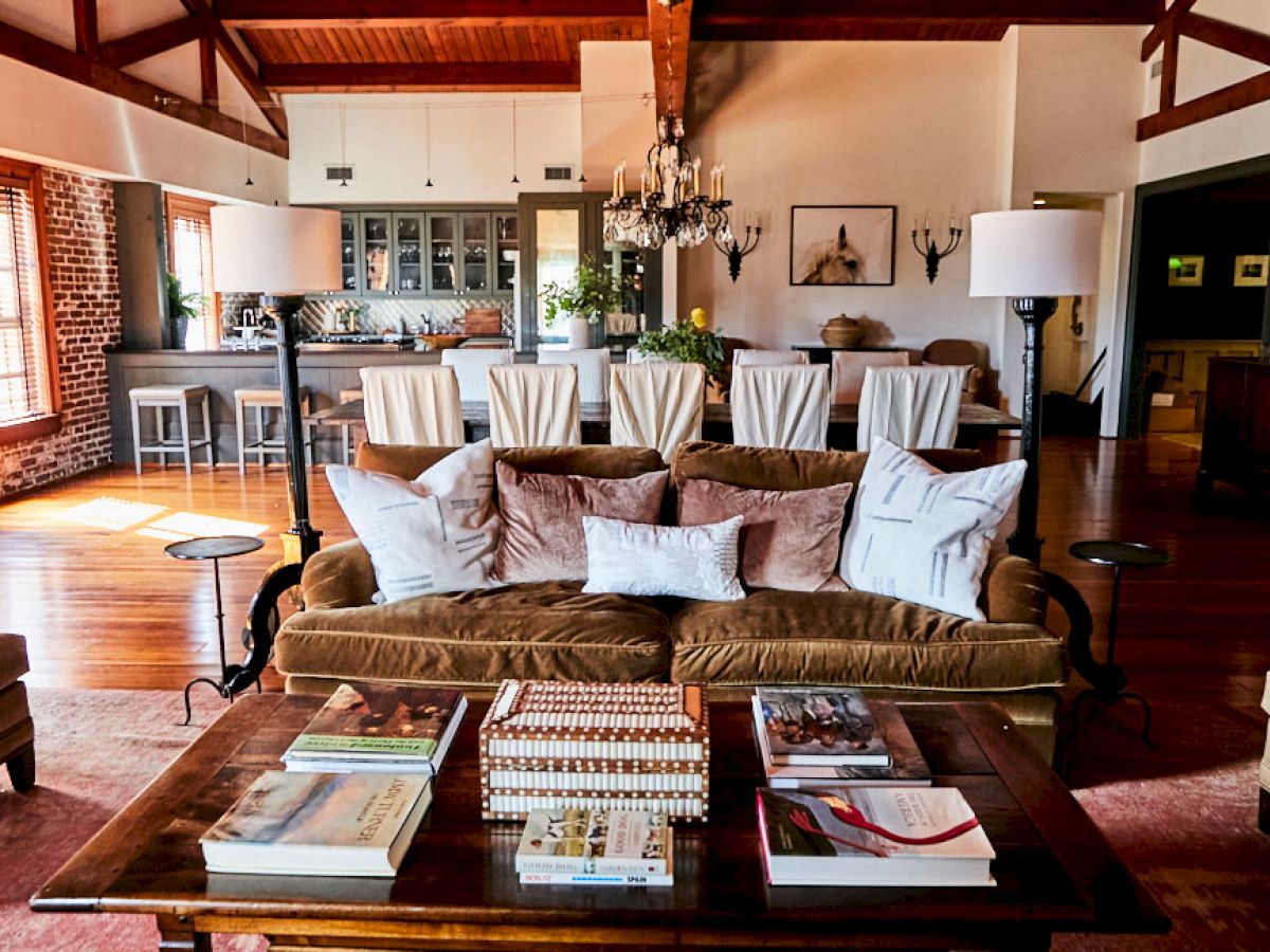 A stylish open-plan living room and kitchen with a brown sofa, white chairs, brick wall, wooden floors, and a chandelier, cozy and airy.