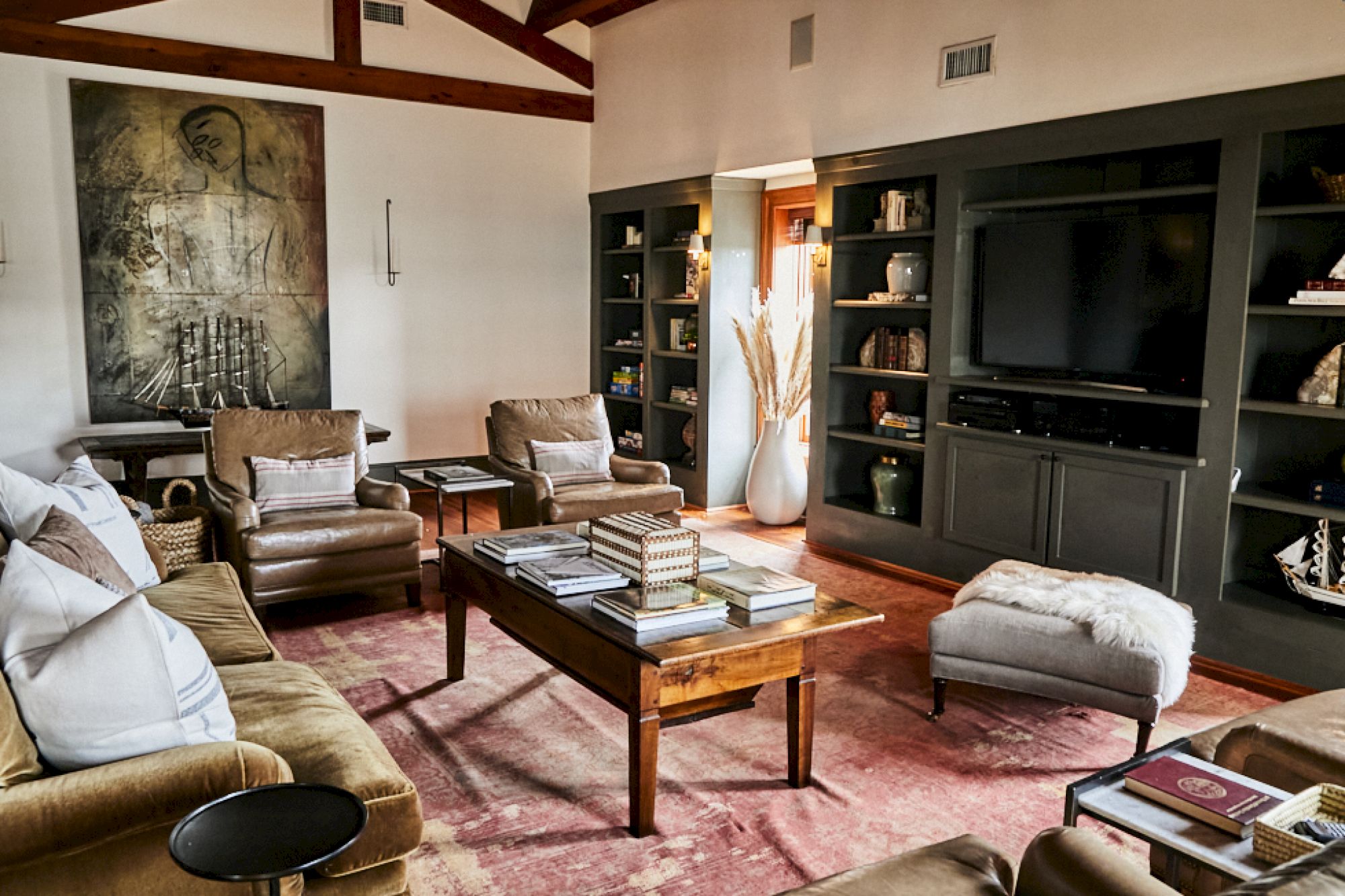A cozy living room with leather sofas, a wooden coffee table, built-in dark shelves, a large TV, soft lighting, and a pink area rug, inviting and stylish.