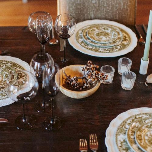 A decorated dining table with ornate plates, wine glasses, candles, and a bowl of berries for a festive meal.