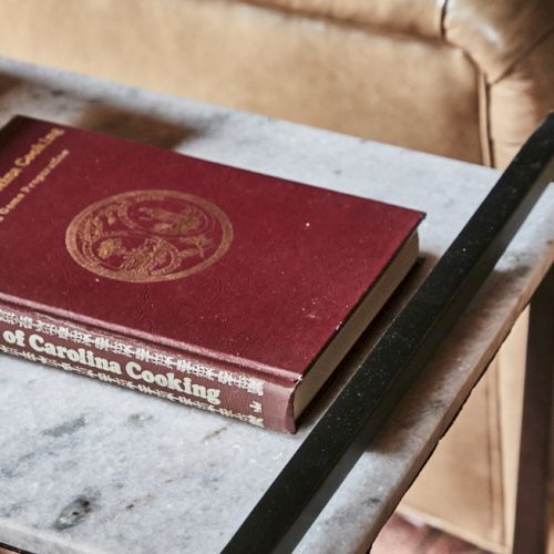 A red notebook with a white label rests on a desk next to a wooden surface and a laptop, suggesting study or writing.