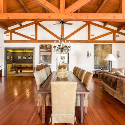 A bright kitchen or dining area with wooden beams, shelves, and warm lighting; a person is cooking or serving at an island.